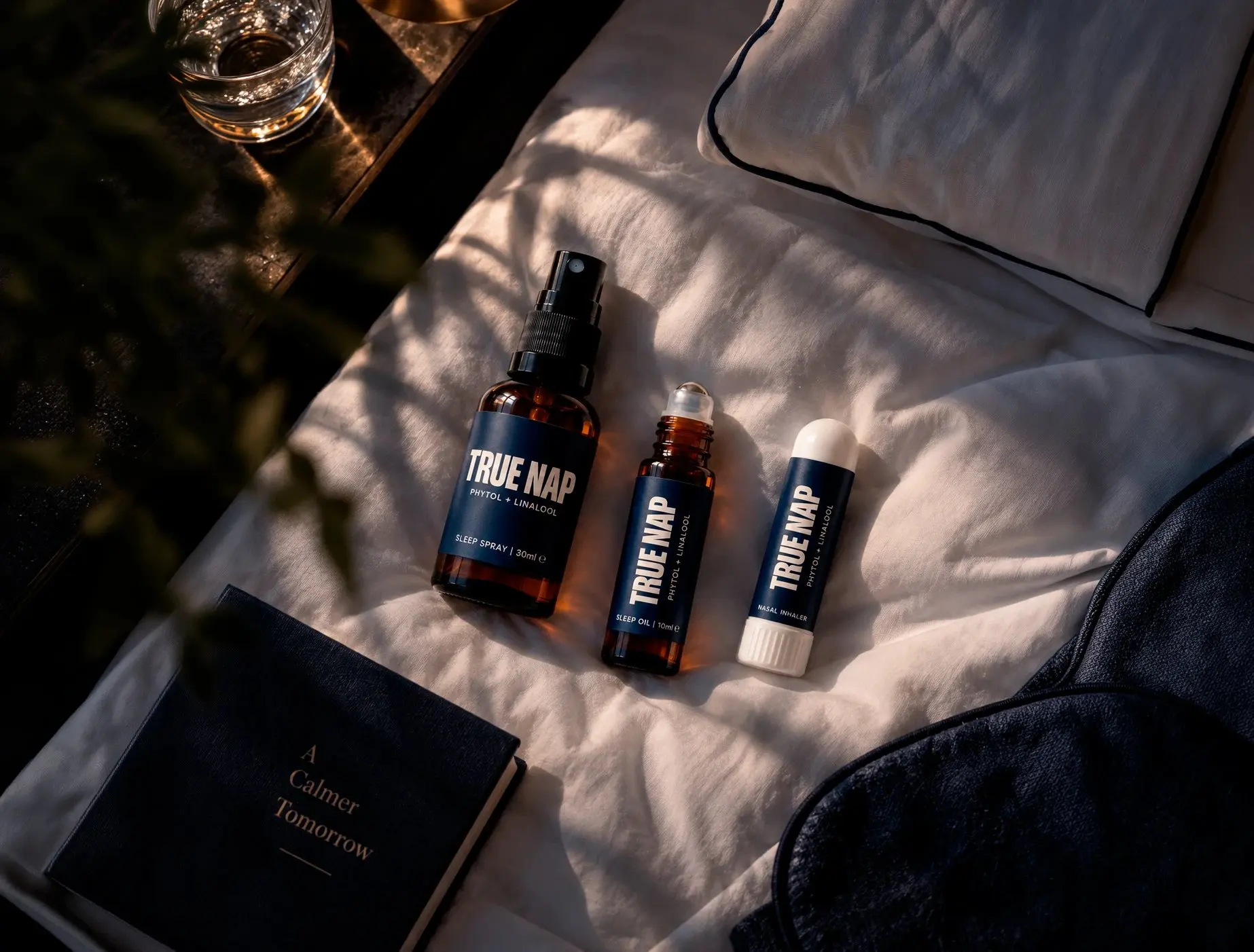 TRUE NAP sleep spray, roll-on oil and inhaler on a hotel bed in the late-afternoon light